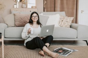 Home Happy woman enjoying coffee while using a laptop in a cozy living room setting.